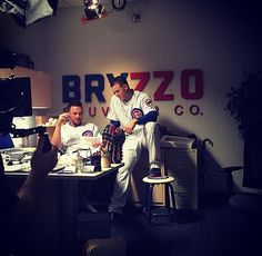 two baseball players sitting at a desk in front of a camera and another man standing next to him