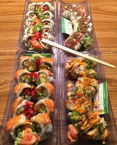 four plastic trays filled with different types of sushi and rice rolls on top of a wooden table