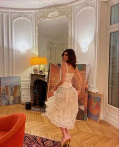 a woman in a white dress is walking through a room with paintings on the wall