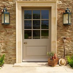 the front door to a stone house with potted plants on the doorstep and light fixtures