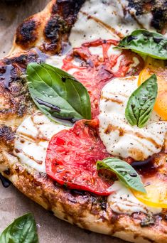 a pizza with tomatoes, basil and mozzarella on it sitting on a piece of parchment paper