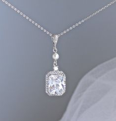 Classically elegant and sophisticated! Emilia cz crystal bridal necklace made in a radiant cut with a frame of tiny cz crystals for a beautiful sparkling accessory that will suit your dress, whatever style. The 18K rhodium setting has delicate carving around the sides so your necklace is pretty from all aspects!A Swarovski pearl in your custom color adds a personalized touch your Emilia necklace.Measures: 2" (5 cm) top to bottom. 0.5" (1.2cm) widest point.All components are  rhodium plated sterl Wedding Crystal Necklace With Brilliant Cut, Classic Bridal Necklace With Cubic Zirconia For Wedding, Exquisite Crystal Necklaces For Weddings, Exquisite Crystal Wedding Necklaces, Classic Crystal Bridal Necklace For Wedding, Exquisite Crystal Wedding Necklace, Elegant Crystal Bridal Necklace, Elegant Bridal Necklace With Rhinestones For Wedding, Exquisite Crystal Bridal Necklace For Wedding