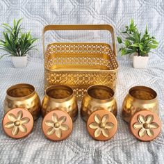 a set of four gold colored metal cups and saucers on a white tablecloth with potted plants in the background