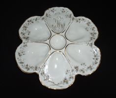 a white and gold flower shaped dish on a black tablecloth with flowers in the center