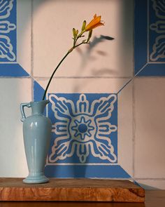 a single flower in a blue vase on a wooden table next to a tile wall