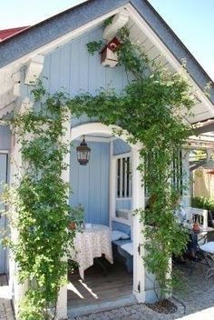 a small blue house with ivy growing on it's roof and door, next to an outdoor dining area