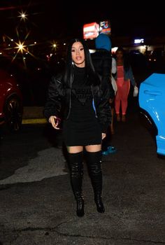 a woman in black dress and thigh high boots standing next to a blue car at night