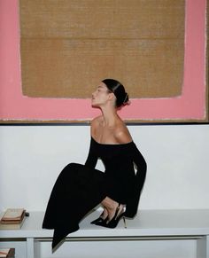 a woman sitting on top of a white bench next to a pink and brown painting