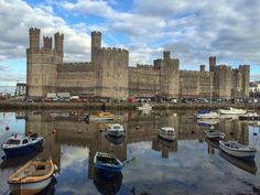 there are many small boats in the water next to this castle and it's reflection