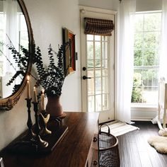 a room with a table, mirror and plants on it in front of the door