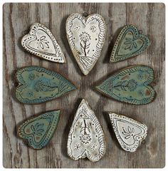 six handmade heart shaped ceramic ornaments on a wooden surface with white and blue designs