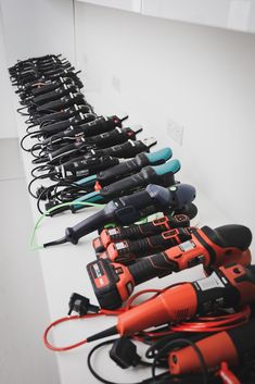 many different types of tools lined up on a white table with black and orange cords