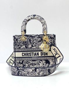 The Lady D-Lite bag combines classic elegance with House modernity. The style is fully embroidered with the blue Toile de Jouy motif. The front features a 'CHRISTIAN DIOR PARIS' signature while the thick 'D.I.O.R.' charms in pale gold-finish metal enhance the silhouette. Equipped with a wide, reversible and removable embroidered shoulder strap, the medium Lady D-Lite bag can be carried by hand or worn crossbody. Dimensions: 24 x 20 x 11 cm. Lady D Lite Bag, Christian Dior Paris, Blue Toile, Womens Designer Bags, Christian Dior Couture, The Lady, Lady Dior Bag, Office Fashion, Arm Candy