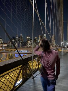 a woman walking across a bridge at night with the city lights in the back ground