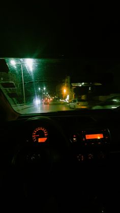 the dashboard of a car at night with street lights in the distance and cars driving down the road