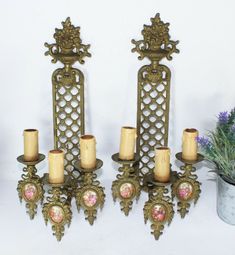 two metal candelabras with candles on them next to a potted plant