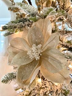 a white christmas tree with gold and silver decorations on it's branches, including a large poinsettia ornament