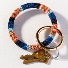 two bracelets with keys attached to them sitting on a white cloth surface, one is blue and the other is orange