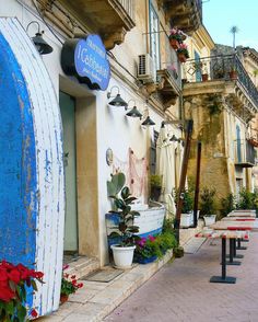 a row of benches sitting next to each other on a sidewalk near buildings with flowers growing out of them