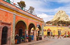 an orange building with people sitting at tables in front of it and mountains in the background