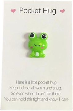 a green frog brooch sitting on top of a piece of paper with the words pocket hug written below it