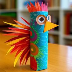 a colorful bird made out of paper sitting on top of a wooden table next to a bookshelf