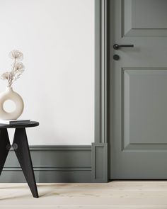 a vase sitting on top of a black table next to a gray door and white wall