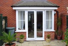 a brick house with white doors and windows on the outside, surrounded by potted plants