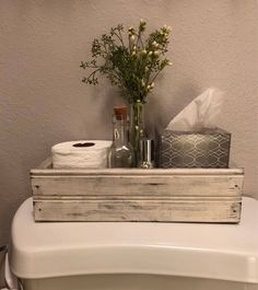 a white toilet sitting in a bathroom next to a wooden tray filled with tissues and flowers