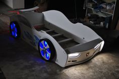 a white bed with blue wheels and lights on the bottom is sitting in a garage