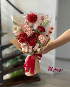 a person holding a bouquet of flowers in their hand with red ribbon on the bottom