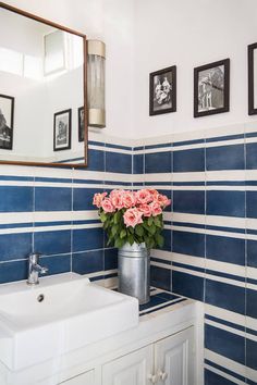 a bathroom with blue and white tiles, pink roses in a metal bucket on the sink