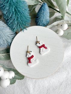 small white snowman earrings with red ribbon on them next to blue christmas tree branches