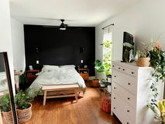 a bed room with a neatly made bed and lots of plants on the dressers