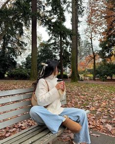 a woman sitting on top of a wooden bench in the park holding a cup of coffee