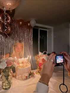 a woman sitting at a table in front of a cake with candles on it and people taking pictures