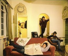 three people sitting in a living room with newspapers on the couch and one person standing up