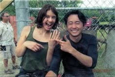 two people sitting next to each other in front of a chain link fence and smiling