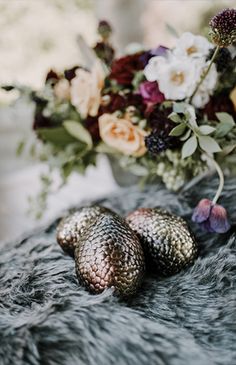 two metal objects sitting on top of a fur covered surface next to flowers and foliage