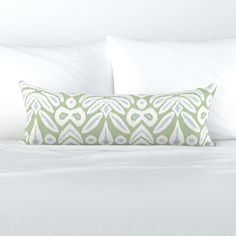 a green and white pillow sitting on top of a bed next to two pillows in front of it