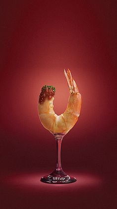 a glass with shrimp on it sitting in front of a red background and the image appears to be half eaten