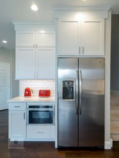 a kitchen with white cabinets and stainless steel refrigerator freezer combo in the center, along with hardwood flooring