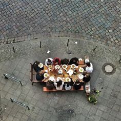 a group of people sitting around a wooden table on top of a stone floored area