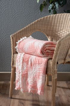 a wicker chair with two blankets folded on it and a potted plant in the background