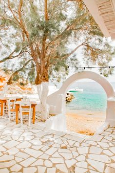 an outdoor dining area with tables and chairs on the beach next to a large tree