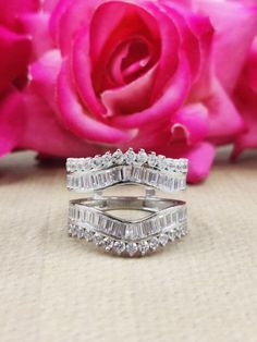 two wedding rings sitting on top of each other next to a pink rose and petals