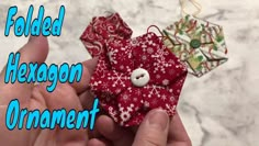 two hands are holding fabric ornament pieces with the words folded hexagon ornament on them