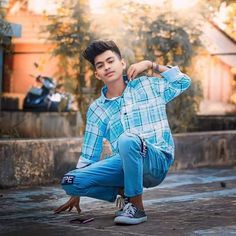 a young man kneeling on the ground with his hands behind his head and wearing blue pants