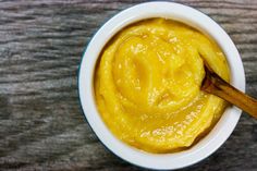 a wooden spoon in a white bowl filled with yellow sauce on top of a table