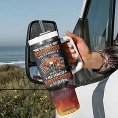 a person holding a coffee cup in front of a car with the ocean in the background